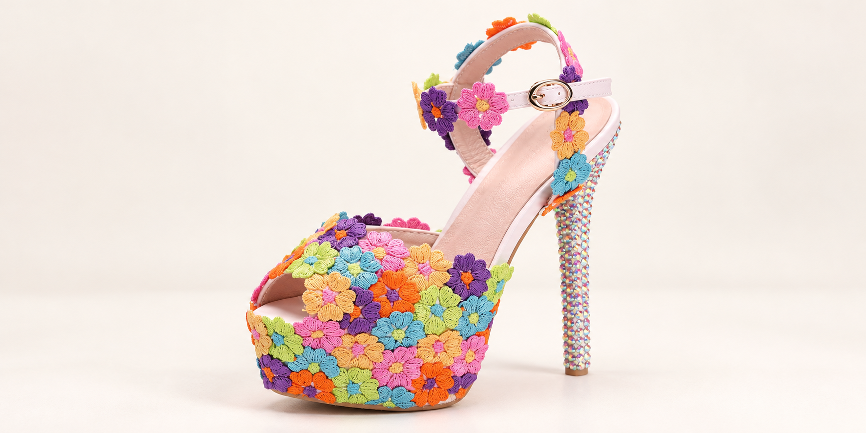 Three-quarter view of a rainbow floral platform sandal showing the open toe, pink insole, round gold-tone buckle and rhinestone-covered stiletto heel.