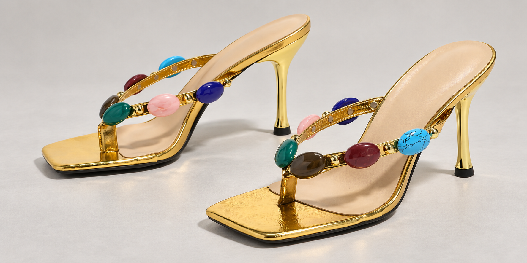Wide close-up of gold Gem-Embellished thong sandals showing the oval stones, narrow straps, square toes and slim heels.